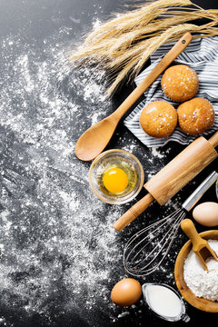 Baking ingredients. Bowl, eggs, flour, eggbeater, rolling pin and eggshells on black chalkboard from above.