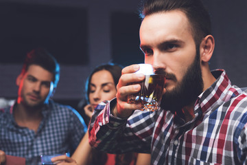 A young guy with a beard drinks a cocktail with whiskey while playing poker.