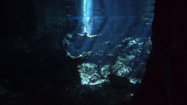 half underwater shot, man in swimsuit with fins dive in stream of sun and many bybbles in cenote cave dos ojos 