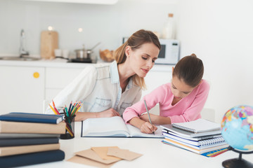 Obraz na płótnie Canvas Mom helps my daughter do her homework in the kitchen.