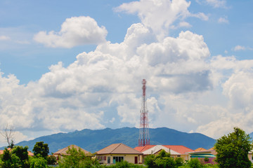 Obraz premium Telecommunications tower in the village with mountainous background and clouds in the sky.