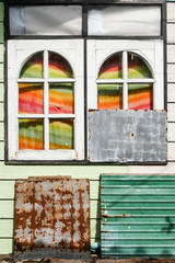 Abstract composition with wooden rounded windows, rusty metal plate and colored curtains with sun light in slum area in Thailand, colorful house facade