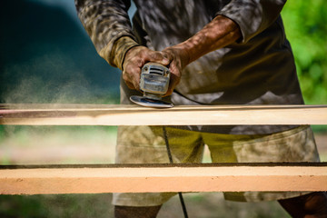 Joiner works with an electric scrubber and processes wooden products.Carpenter with handheld electric scrubber .in the hands on the woodwork.