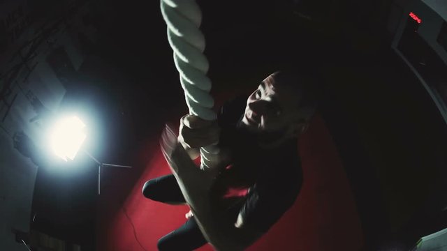 Muscular man climbs rope at gym