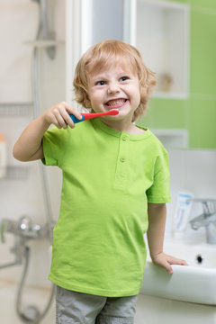 Happy kid or child brushing his teeth in bathroom. Dental hygiene.