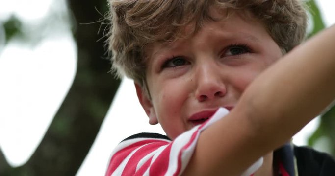Child crying in tears. Real life authentic candid sobbing of a tearful child on top of a tree. Inconsolable crying young boy is sobbing in 4k