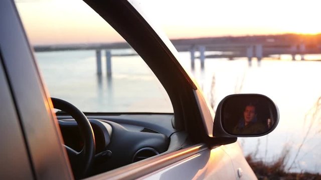 A man is sitting in the car in the parking lot and admiring the beautiful view and sunset in the open car window. slowmotion, HD, 1920x1080
