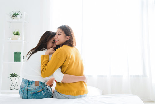 Back view of women lesbian happy couple waking up in morning, sitting on bed, stretching in cozy bedroom, looking through window. Funny women after wakeup. Lesbian couple together indoors concept.