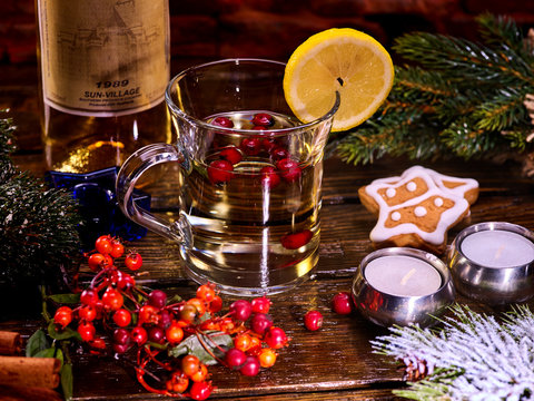 Tea cup glass with warming beverage and berries and alcohol. Christmas still life with mug decoration lemon slice hot drink and bottle white wine. Bottle has label.