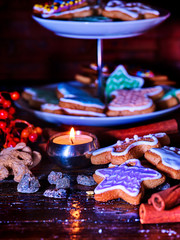 Candle light table with Christmas gingerbread cookies and cinnamon stick and star sweets are on decoration tiered cake stand wooden table and burning candles. Xmas still life object.