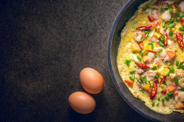 Omelette in frying pan on dark background, top view. garlic and fresh tomatoes. Traditional