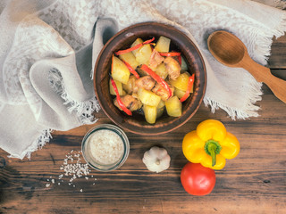 Baked potato with chicken and red pepper. Salt, garlic, tomato and yellow pepper, top view. Roast in the ceramic bowl on the background of wooden table and fabric. Horizontal photo of rustic style.