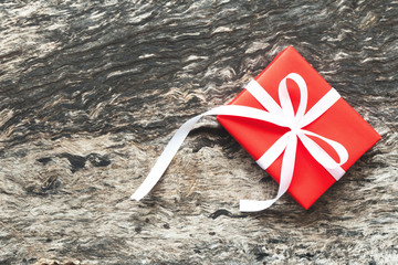 Wrapped red gift box with white ribbon bow on old and rustic wooden background. Christmas, New Year and happy birthday present concept