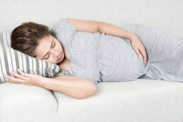 Young beautiful pregnant woman sleeping on gray sofa and pillow at home.