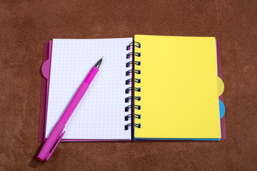 Notepad and ballpoint pen on a brown suede background.