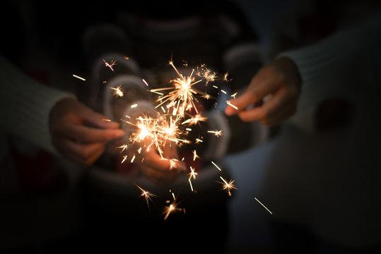 Bright festive Christmas or New Year sparkler in hand toning, showing group of friends having fun.