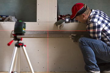 Handyman drawing a line on dry wall with help of laser leveler