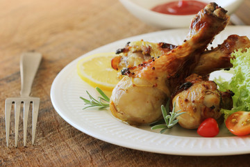 Grilled chicken legs with mustard on wooden table served on white plate with rosemary. BBQ dinner background