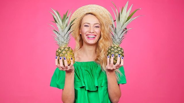 Happy young blonde woman holding a two pineapple on a pink background