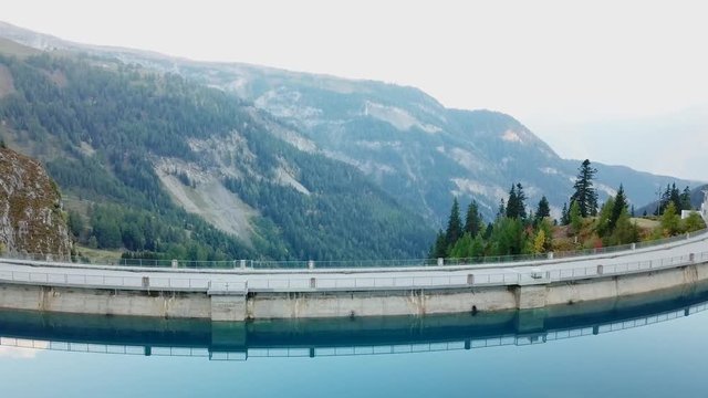 Drone aerial footage of reservoir lake and arch dam for renewable energy power plant in Switzerland Alps, tilting down