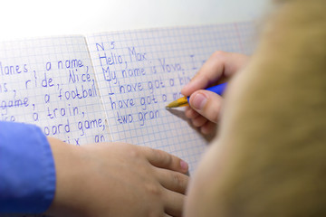 Close-up of boy hand with pencil writing english words by hand on traditional white notepad paper.