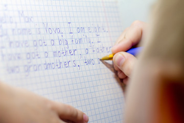 Close-up of boy hand with pencil writing english words by hand on traditional white notepad paper.