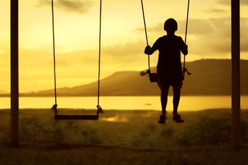 Silhouette of child enjoying the swing outdoors with river and mountain view