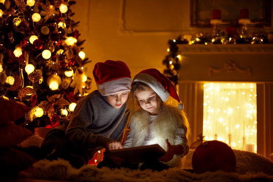 Excited boy and girl sitting near Christmas tree, playing tablet game together.