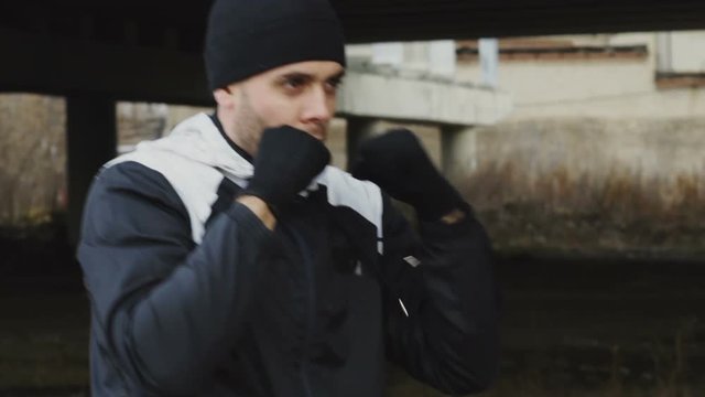Slowmotion of sportive man boxer doing boxing exercise in urban location outdoors in winter