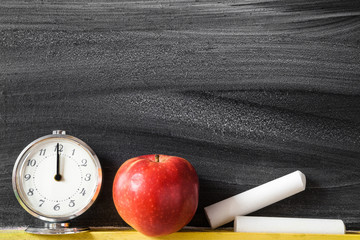 White chalks, red apple and clock at the blackboard in classroom.  Lunch time concept. Empty place...