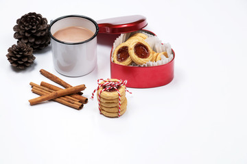 Cup of hot chocolate with cinnamon sticks and christmas cookies with jam in heart shaped red box on white background.