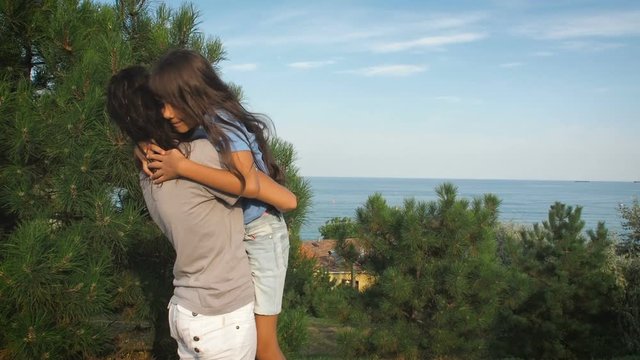 A woman is hugging a child. The daughter hugs her mother against the background of the sea landscape.