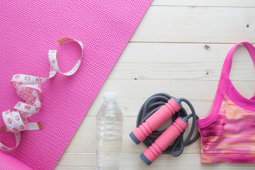 Flat lay, Top view of Healthy concept with sport bra, yoga mat, measuring-tape and sport equipments on wooden background