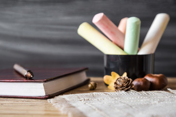 Teacher's colorful chalks with school journal and pen on the wooden table at the blackboard in classroom. Education concept. Empty place for a text.