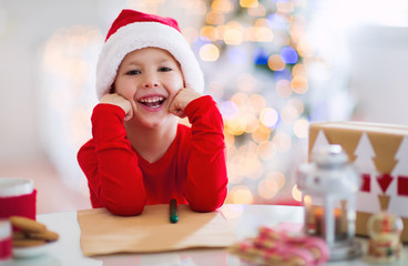 Fototapeta na wymiar Boy writing letter to Santa Claus in red hat near the Christmas tree