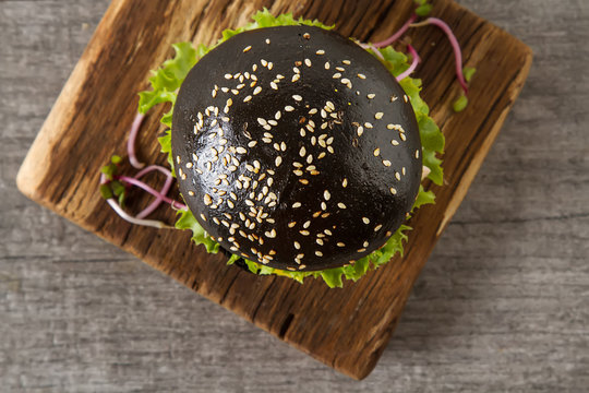 Black burger with salmon fish, lettuce, mustard. Light white background. Fast food.