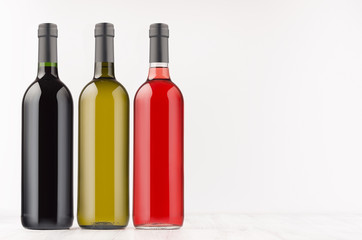 Wine bottles collection different colors - red, green, black- on white wooden board, mock up, copy space. Template for advertising, design, branding identity.