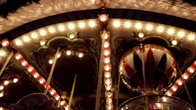 A glowing decoration of rotating carousel on a night. Evening in the amusement park. Old retro merry-go-round is turn s with illuminated light bulbs.