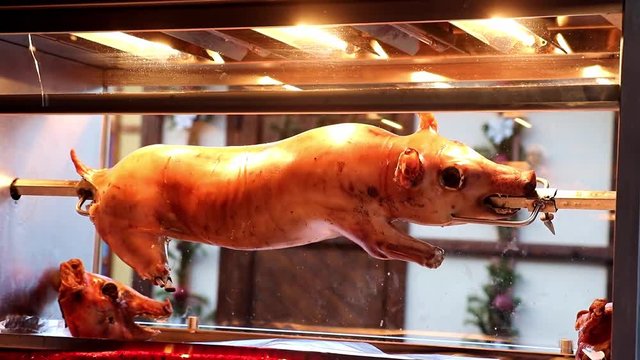 Roasted pig on the street in a glass box. Traditional grilled piglet on the Christmas market. Sucking pig rotate on stick in electric oven outdoors.