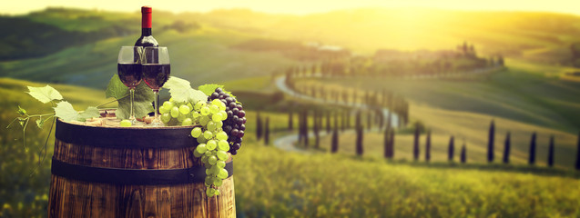 Red wine bottle and wine glass on wodden barrel. Beautiful Tuscany background - obrazy, fototapety, plakaty