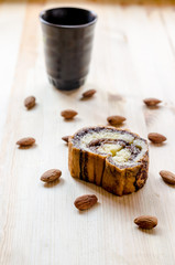 Sweet roll cake and almonds on wooden background