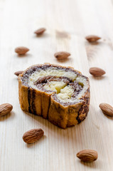 Sweet roll cake and almonds on wooden background