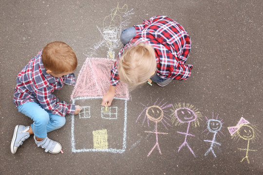 Little children drawing house and family with chalk on asphalt
