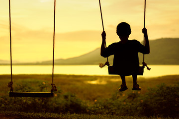 Silhouette of child enjoying the swing outdoors with river and mountain view