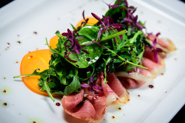 Salad with fried bacon herbs and orange fruit in white plate with black background