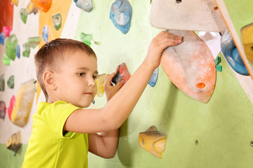 Adorable little boy climbing on wall in gym