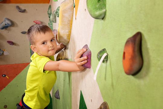 Adorable little boy climbing on wall in gym
