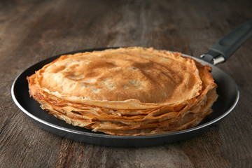 Frying pan with stack of delicious thin pancakes on wooden table