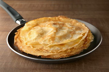 Frying pan with stack of delicious thin pancakes on wooden table