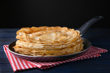 Frying pan with stack of delicious thin pancakes on wooden table